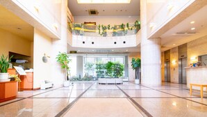 A spacious lobby with a high ceiling, a reception desk, a seating area, and a balcony with plants. - Bright Park Hotel (Kochi)