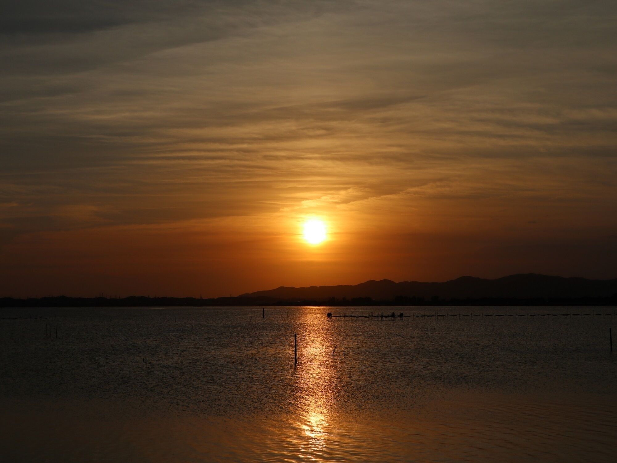 A sunset over a calm body of water with a distant shoreline silhouette.