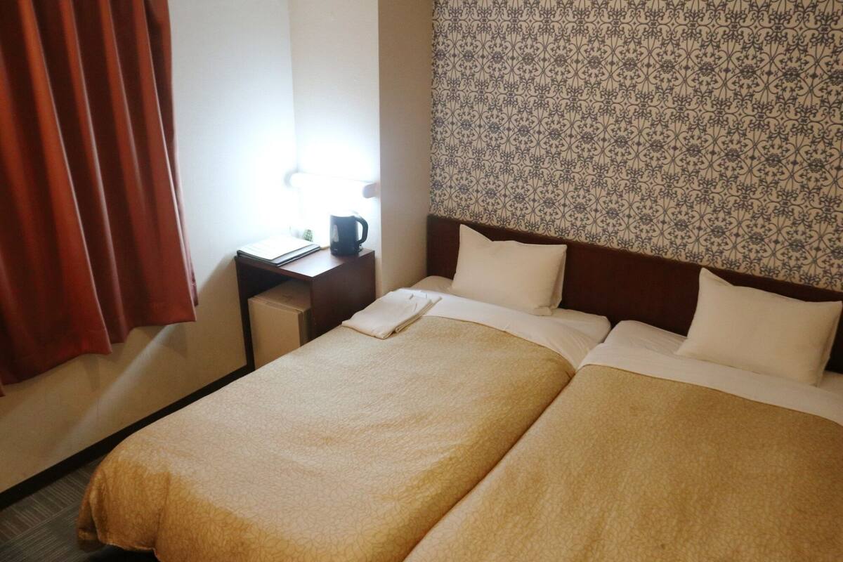 Une chambre d’hôtel avec deux lits, un bureau, une chaise et une tête de lit à motifs.