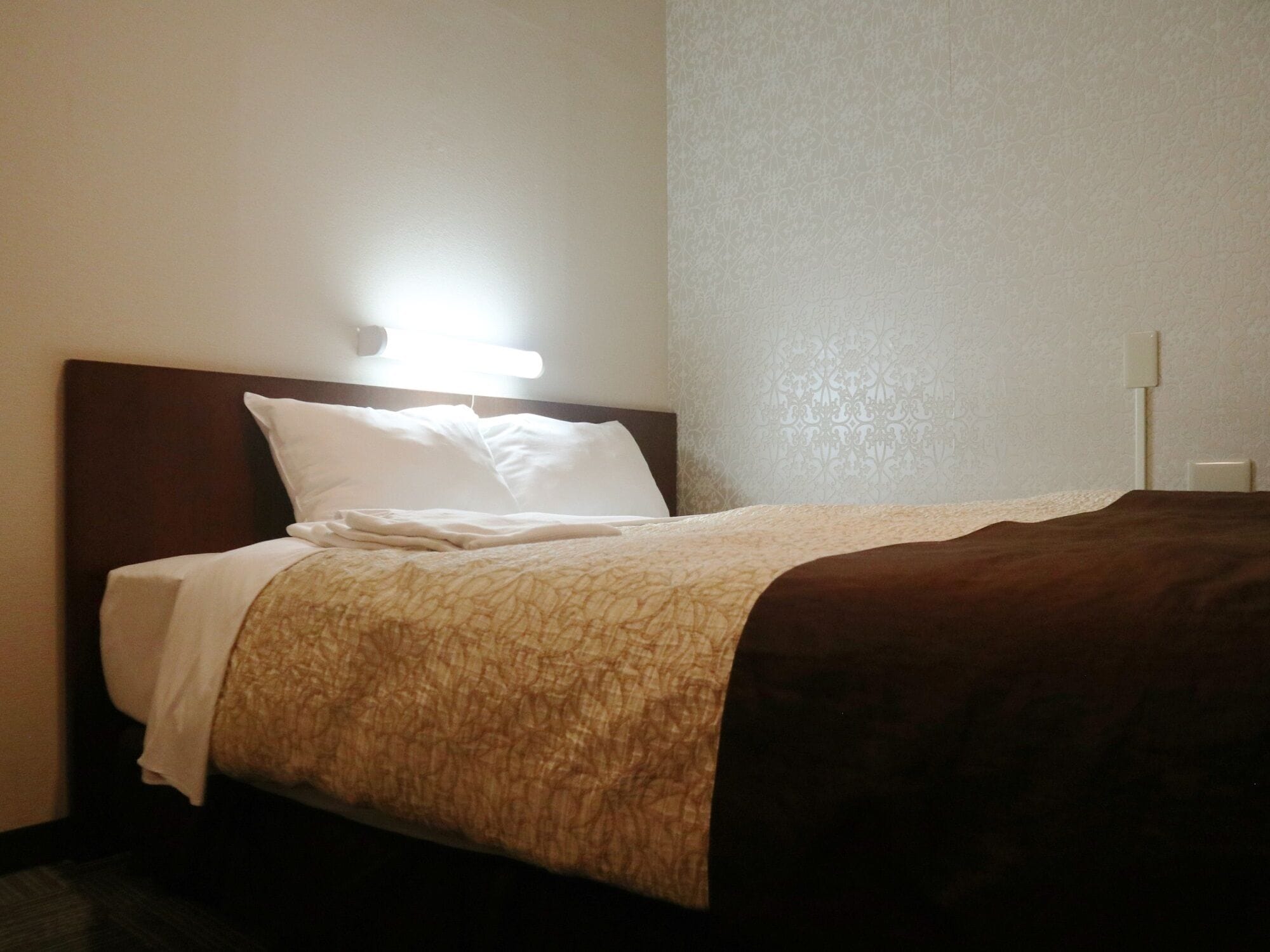 Una cama bien tendida con una colcha marrón y blanca, una almohada blanca y un cabecero.