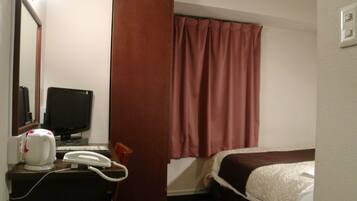 Una habitación de hotel con cama, escritorio con teléfono, televisión y espejo.
