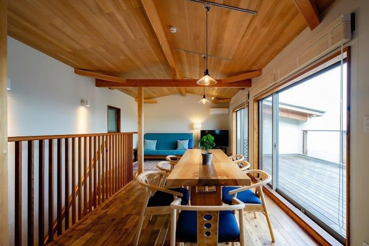 Un interior de madera con comedor, sofá y un ventanal grande.
