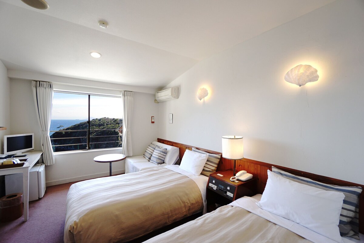 Habitación de hotel con dos camas, un escritorio con computadora, una lámpara y un teléfono en la mesita de noche.