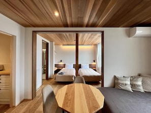 A modern hotel room with a wooden ceiling, a large bed, a seating area with a wooden table, and a separate sleeping area with a smaller bed. - Garden Villa Shirahama (Shimoda)