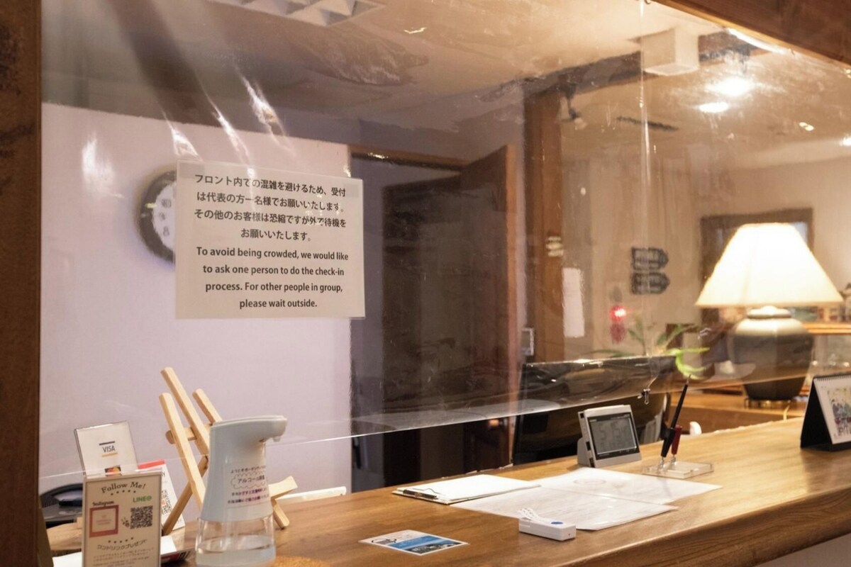 Una recepción con mostrador de check-in, un reloj y un cartel con indicaciones para el registro.