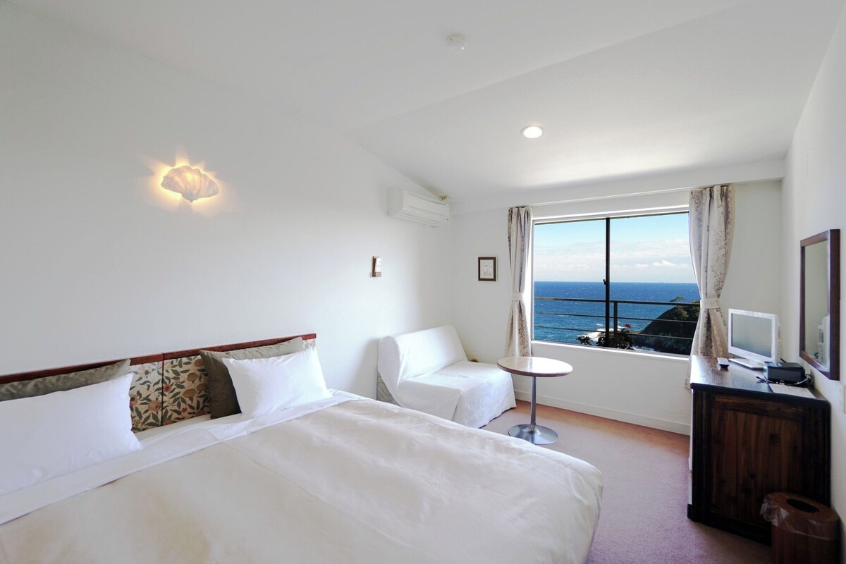 Habitación de hotel con una cama grande, una mesita, una silla y vista al mar.