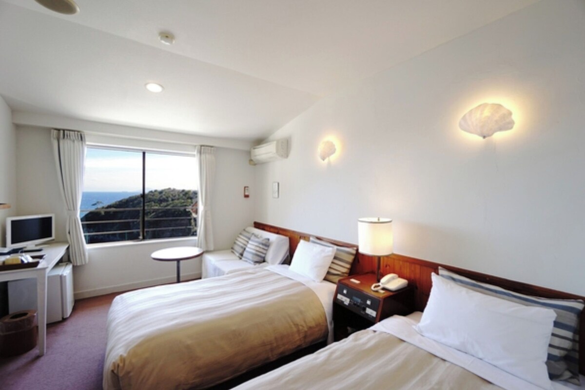 Habitación de hotel con dos camas, un escritorio con computadora, una mesita y vista al mar.