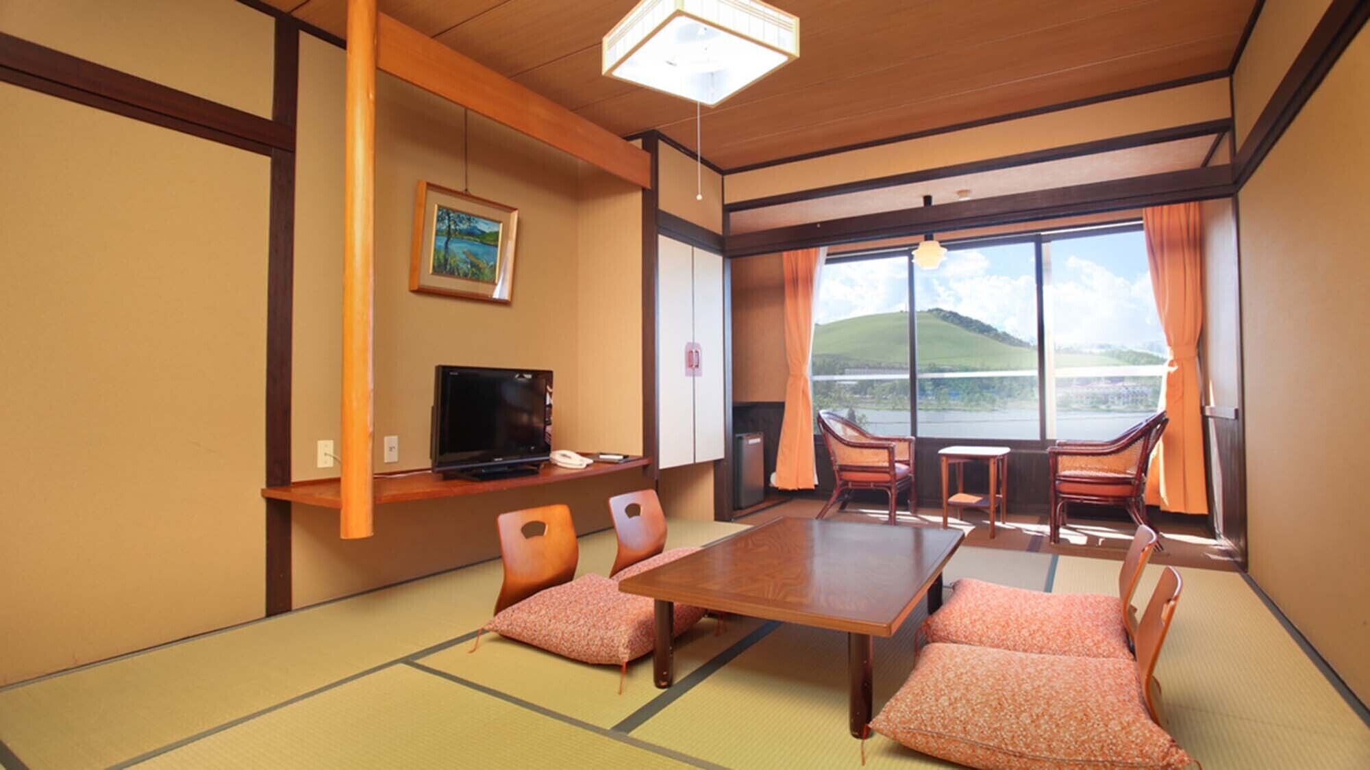 Una habitación japonesa tradicional con suelo de tatami, televisión, escritorio y vistas a un lago.