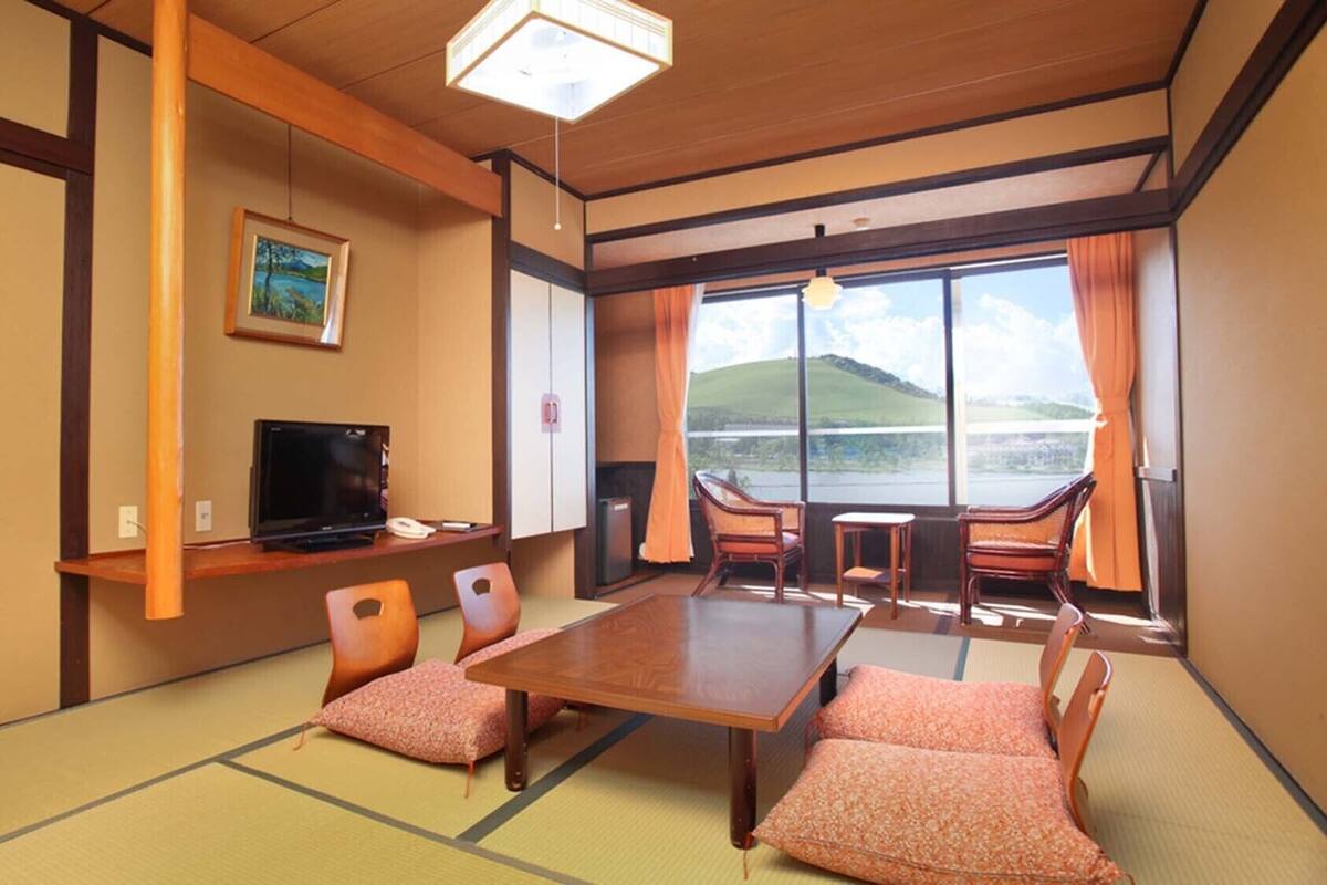 A traditional Japanese-style room with tatami flooring, a television, a desk, and a view of a lake.