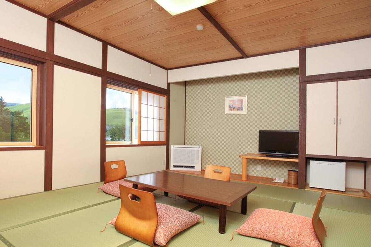 A traditional Japanese-style room with tatami flooring, a low table, chairs, a television, and a cabinet.