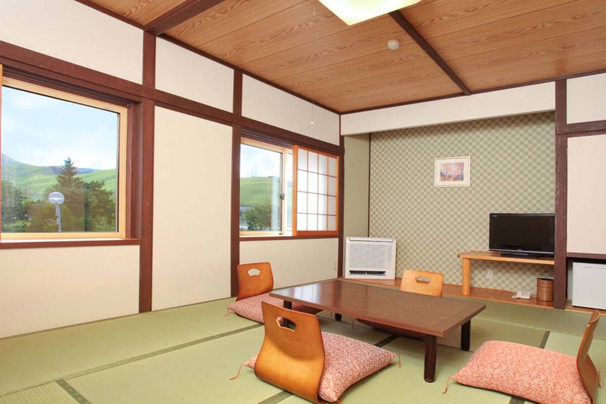 A traditional Japanese room with tatami flooring, a low table, chairs, a television, and a cabinet.