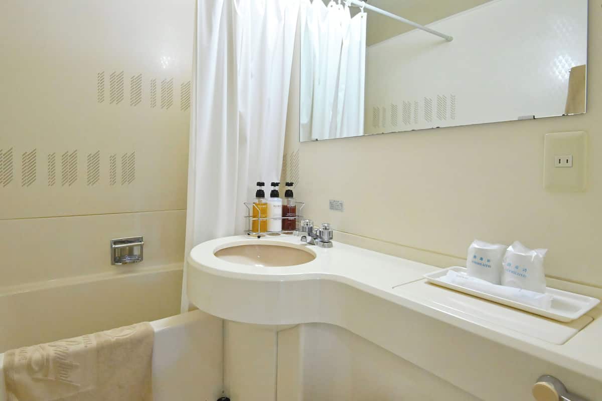 A bathroom with a white sink, a mirror, a towel rack, and toiletries.