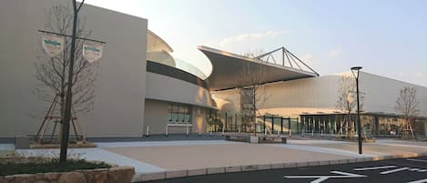A modern building with a curved facade, a glass entrance, and a paved area with directional arrows.