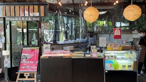 Un puesto de comida con un cartel de menú, una vitrina refrigerada y un letrero que indica servicio para llevar.