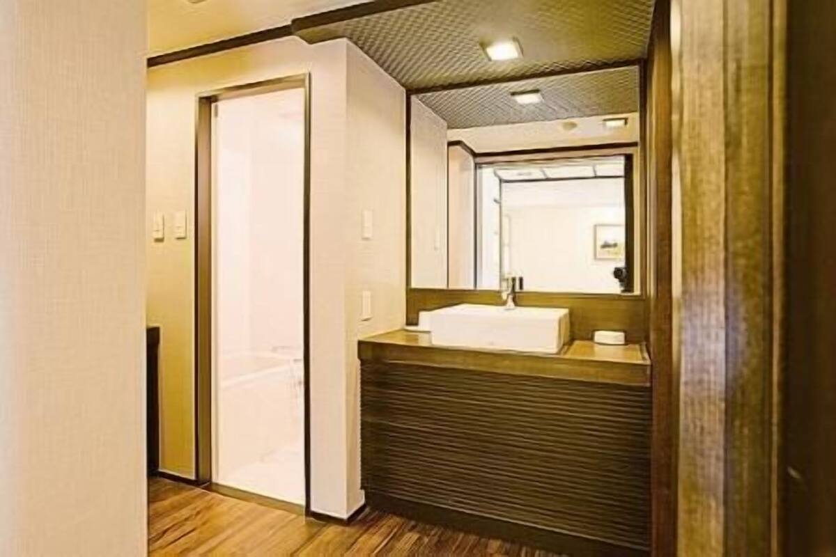 A narrow hallway with a wooden floor, a white door, and a bathroom with a sink and mirror.