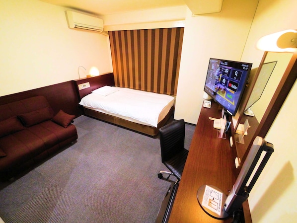 A hotel room with a bed, a sofa, a desk with a computer, and a TV.