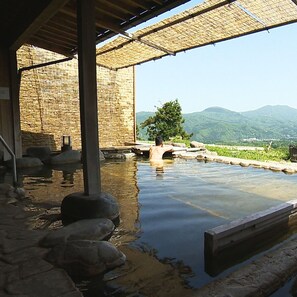 Eine traditionelle Steinbadewanne mit Holzterrasse und einer strohgedeckten Struktur.
