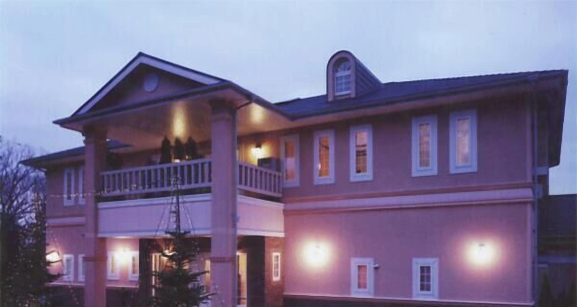 A two-story building with a balcony on the upper floor, multiple windows, and a porch area.
