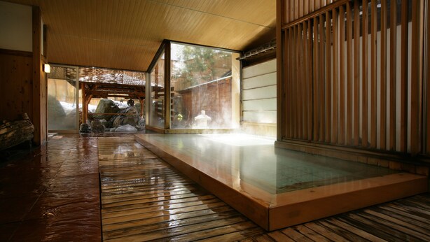 Un onsen japonés tradicional con suelo de madera, un chapuzón de piedra y vistas al exterior a través de una puerta corredera.
