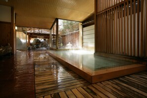 Un onsen japonés tradicional con suelo de madera, un chapuzón de piedra y vistas al exterior a través de una puerta corredera.