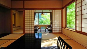 Una habitación japonesa tradicional con suelo de tatami, puertas correderas y vistas a la vegetación.