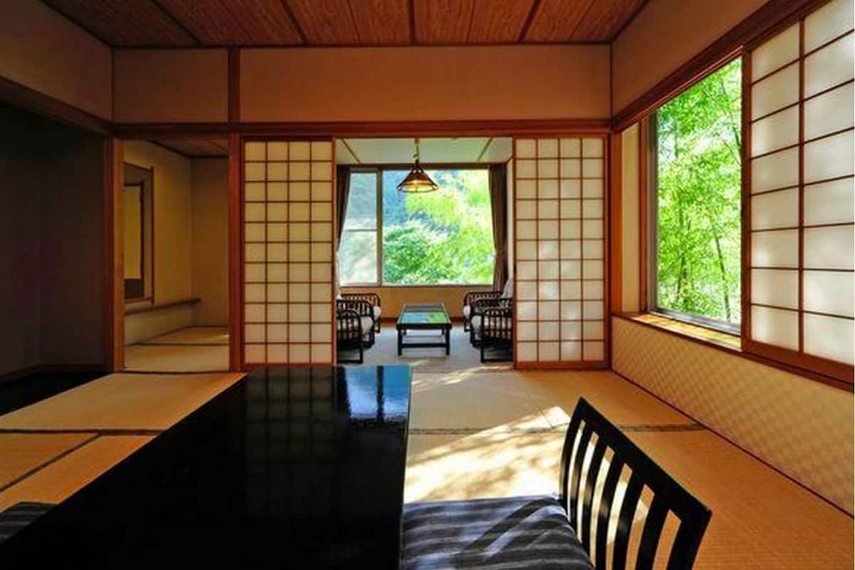 Una habitación japonesa tradicional con suelo de tatami, puertas correderas y vistas a la vegetación.