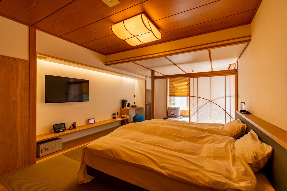 Un dormitorio con cama, televisor, escritorio y ventana con persianas.
