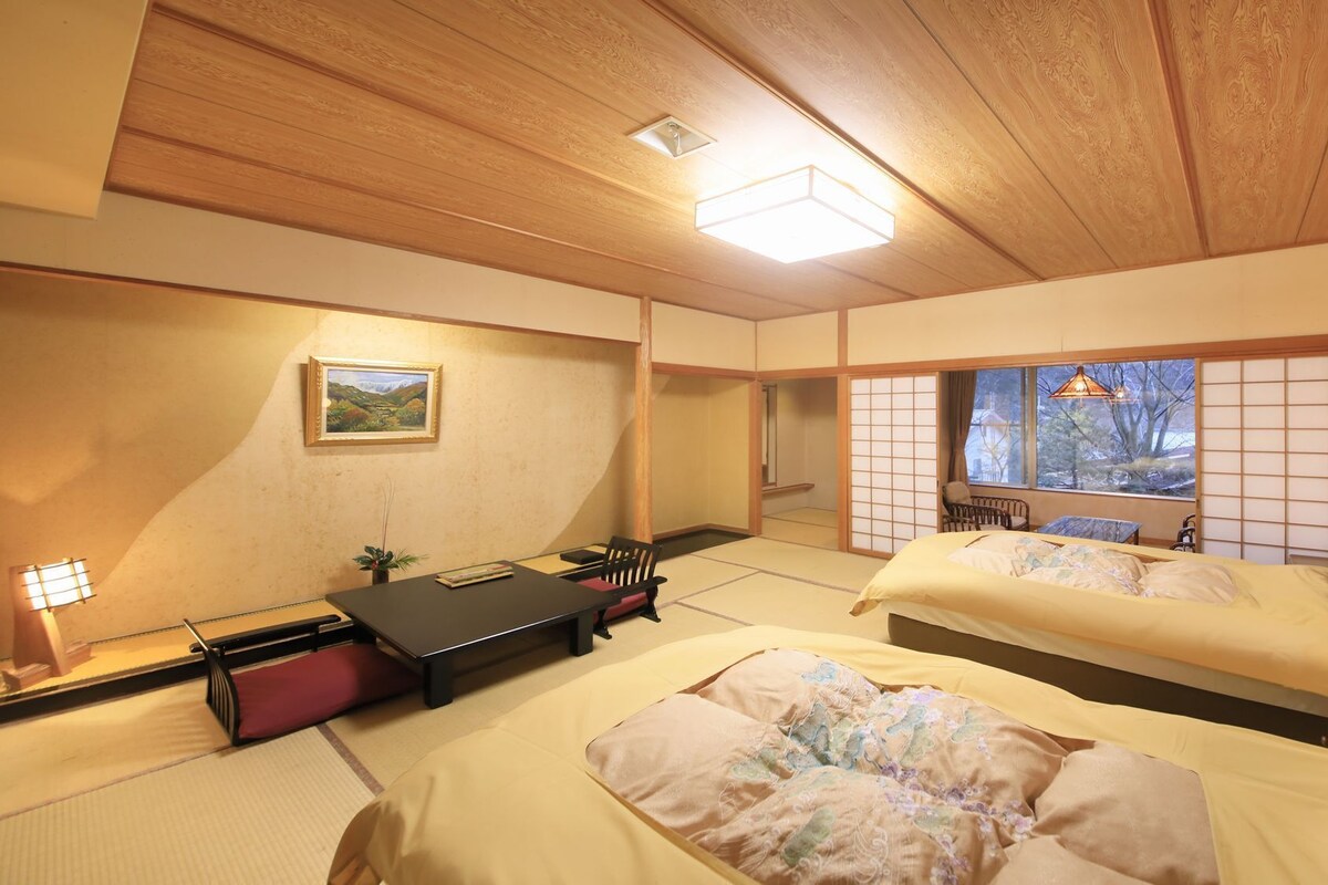 Una habitación tradicional japonesa con suelo de tatami, dos camas, una mesa y vistas al exterior.