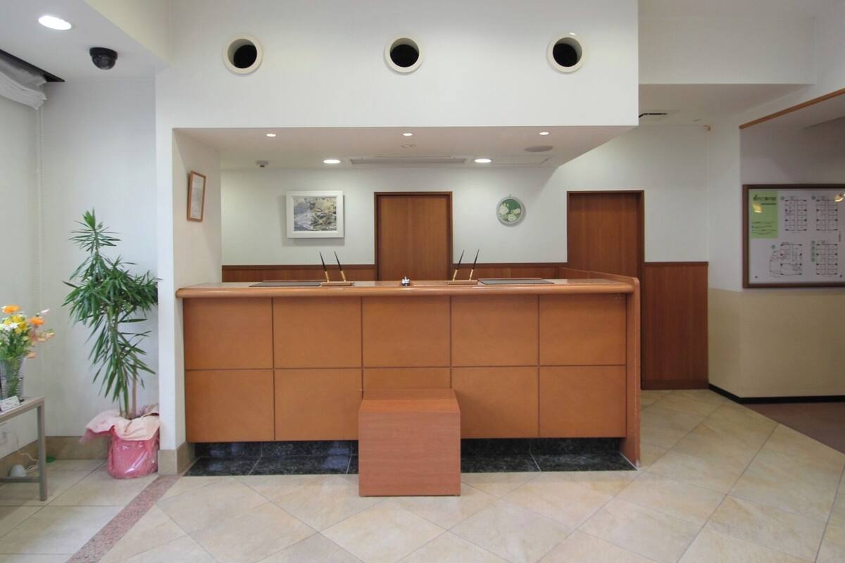 A reception area with a wooden counter, a bench, a potted plant, and a wall-mounted clock.