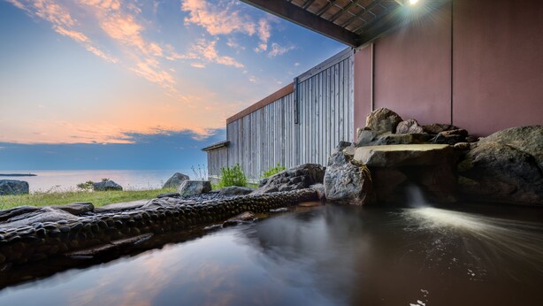 A serene outdoor setting with a stone water feature, a wooden structure, and a view of the water body. - Hotel Grand Mer Sankaiso (Ajigasawa)