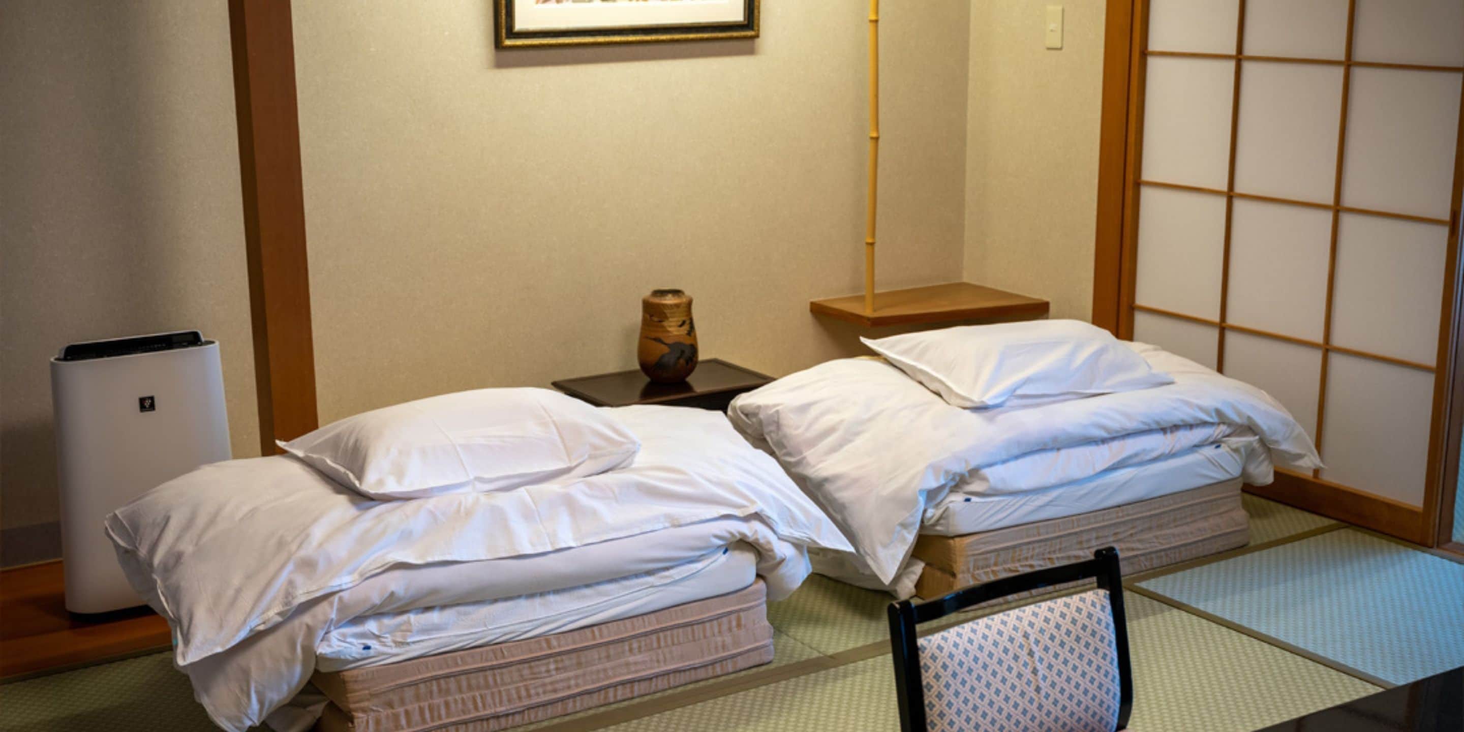 Habitación de hotel con dos camas, una mesita de noche, un pequeño jarrón y un fusuma japonés tradicional.
