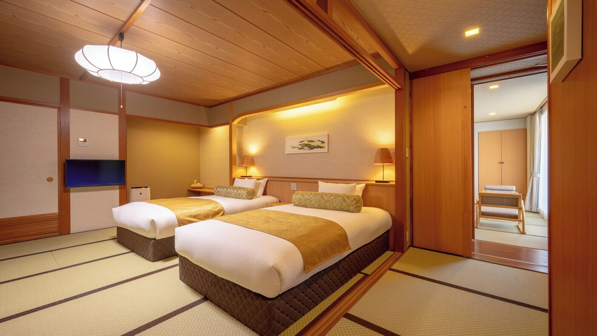 A traditional Japanese-style hotel room with tatami flooring, two beds with matching headboards, a television, and a sliding door leading to a bathroom.