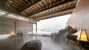 A traditional hot spring bath with wooden benches, a thatched roof, and a view of snow-covered mountains in the background. - Hotel Grand Mer Sankaiso (Ajigasawa)