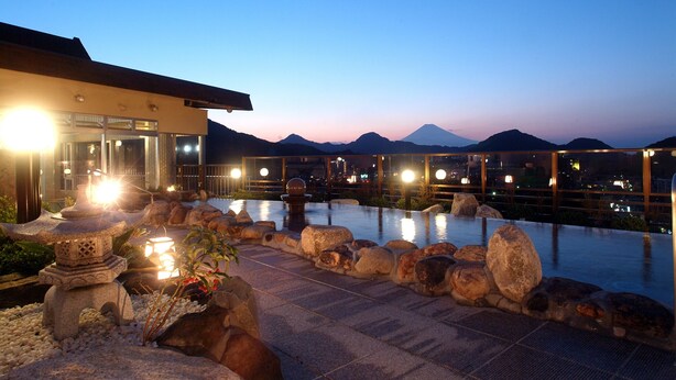 An infinity pool with a stone pathway, a stone lantern, and a mountain view at dusk. - New Hakkeien (Izunokuni)