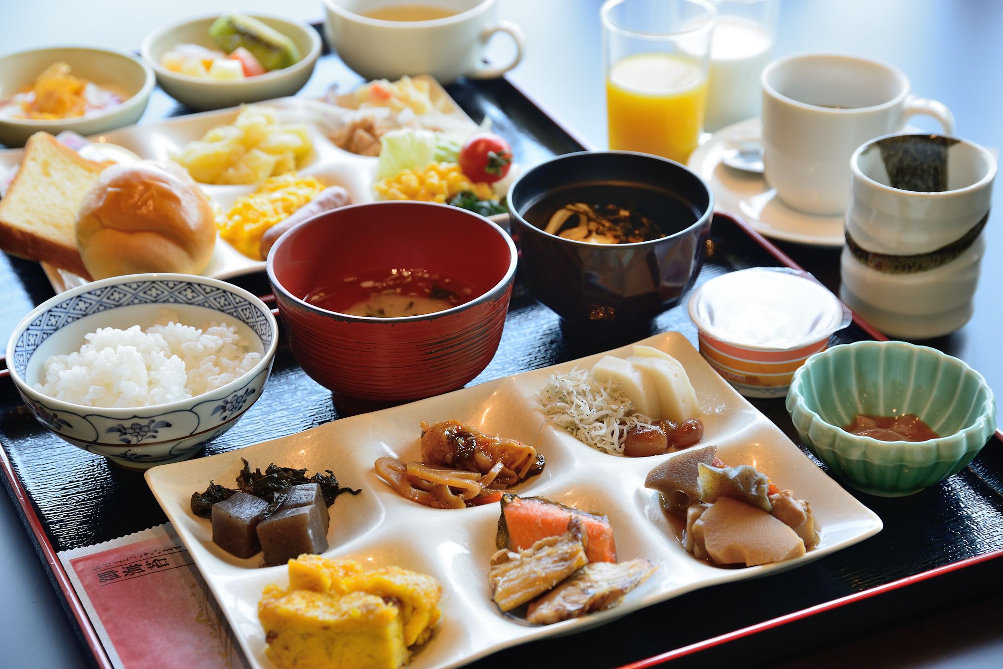A variety of dishes including rice, soup, and meat, served on a tray with cups and a glass of orange juice.