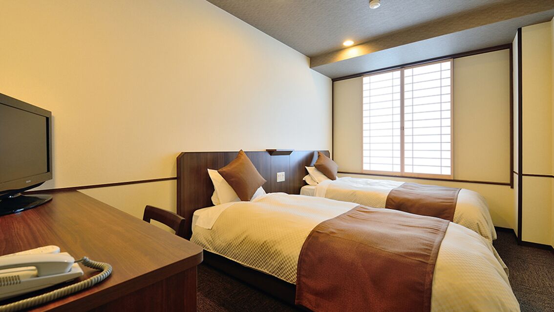 A hotel room with two beds, a desk with a telephone, and a television.