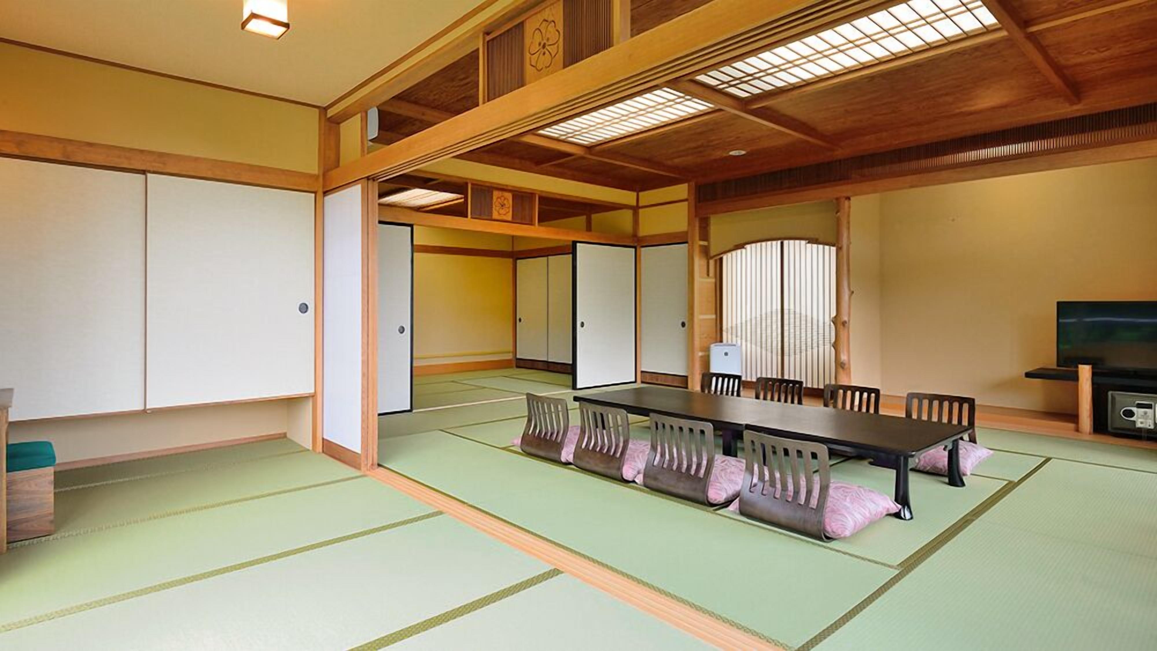 A traditional Japanese room with tatami flooring, a low table with cushions, sliding doors, and a television.