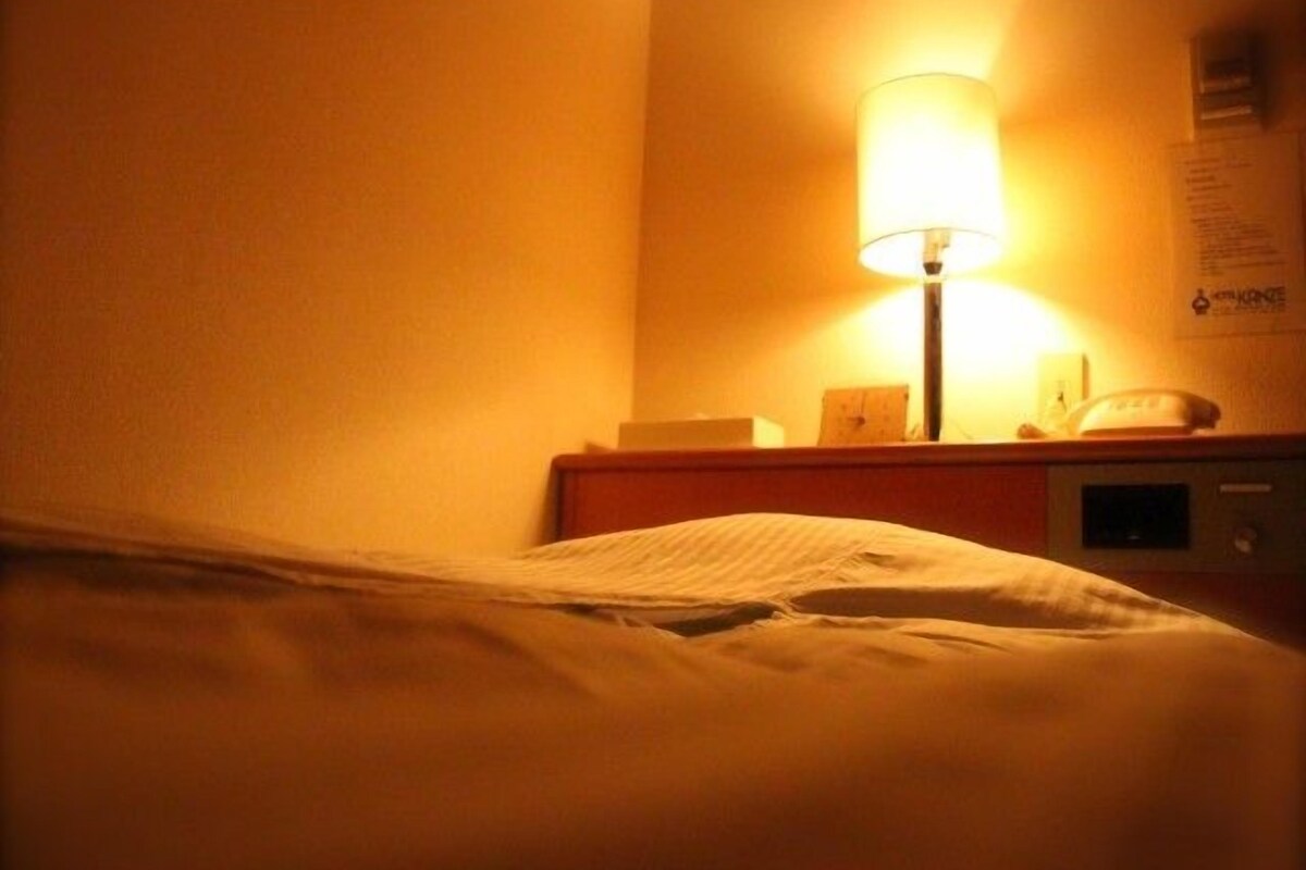 A hotel room with a bed, a nightstand, a lamp, and a wall-mounted sign.