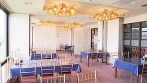 A hotel room with a large bed, a desk, and a chair. There is a window with curtains, and a chandelier hanging from the ceiling.