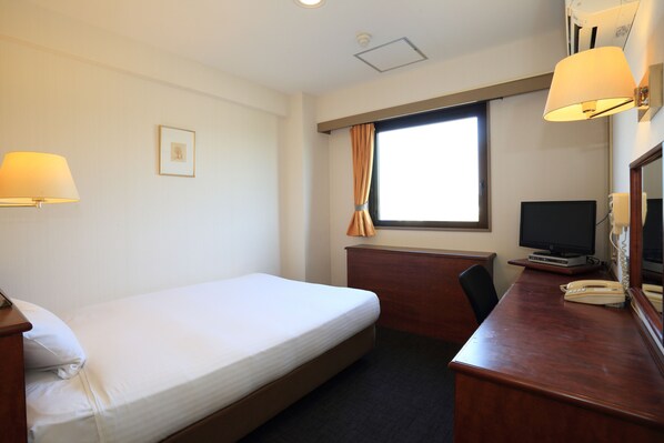 Habitación de hotel con una cama individual, un escritorio con teléfono, televisión y ventana con cortinas.