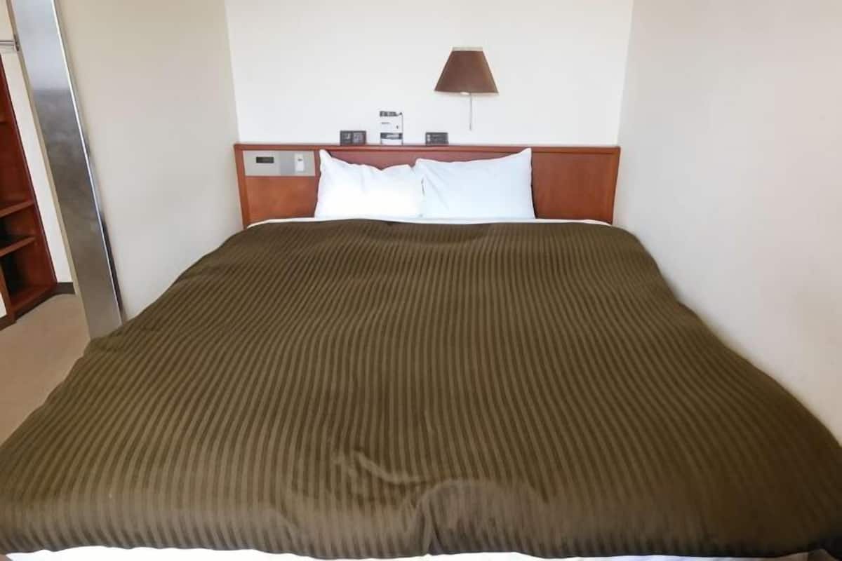 A hotel room with a bed, a nightstand, a lamp, and a digital clock.