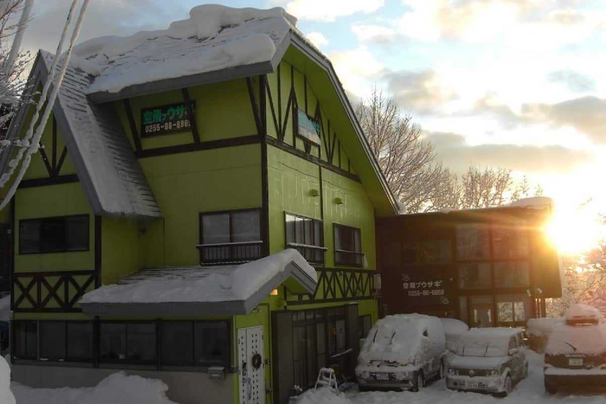 A two-story building with a green facade and a balcony, surrounded by snow-covered cars.