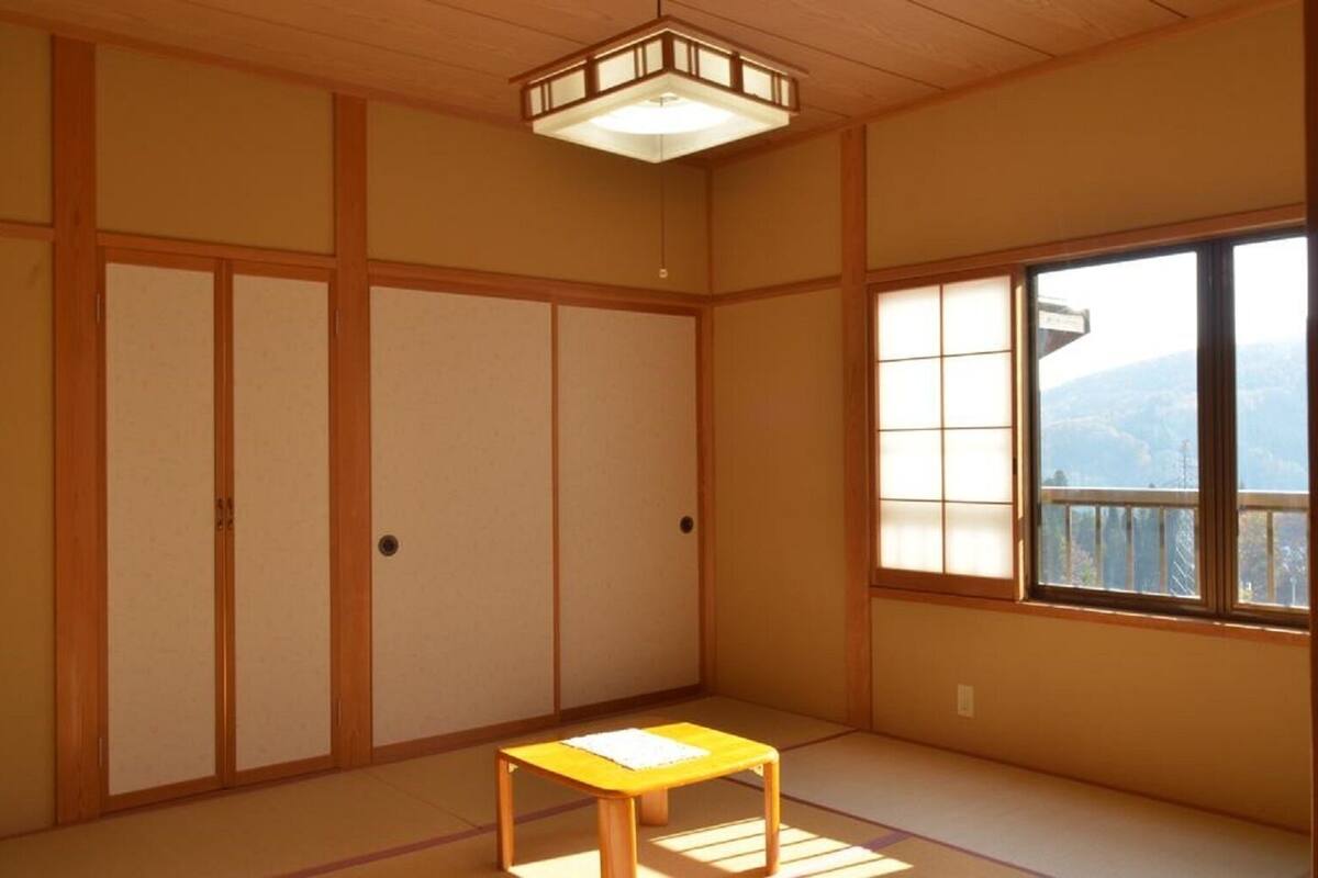 A traditional Japanese room with tatami flooring, sliding doors, a small table, and a window with a view.