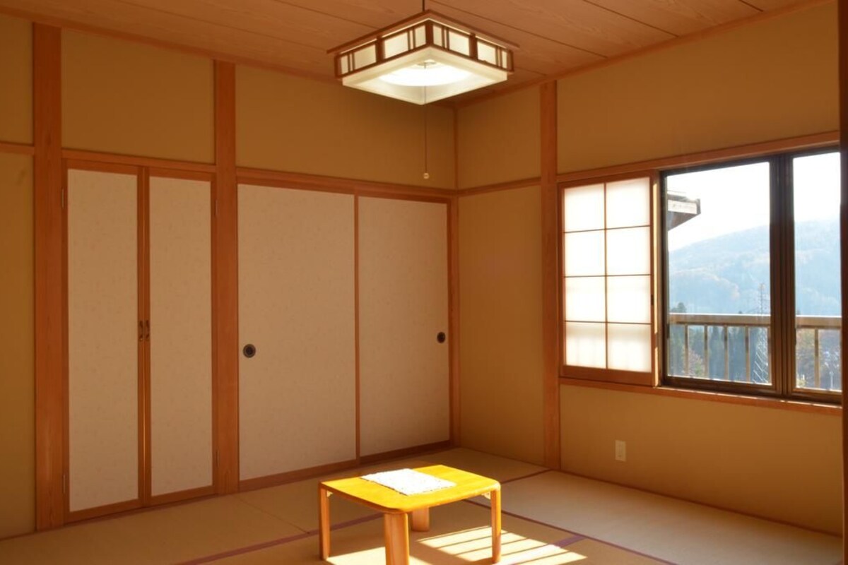 A traditional Japanese room with tatami flooring, sliding doors, a small wooden table, and a window with a view.
