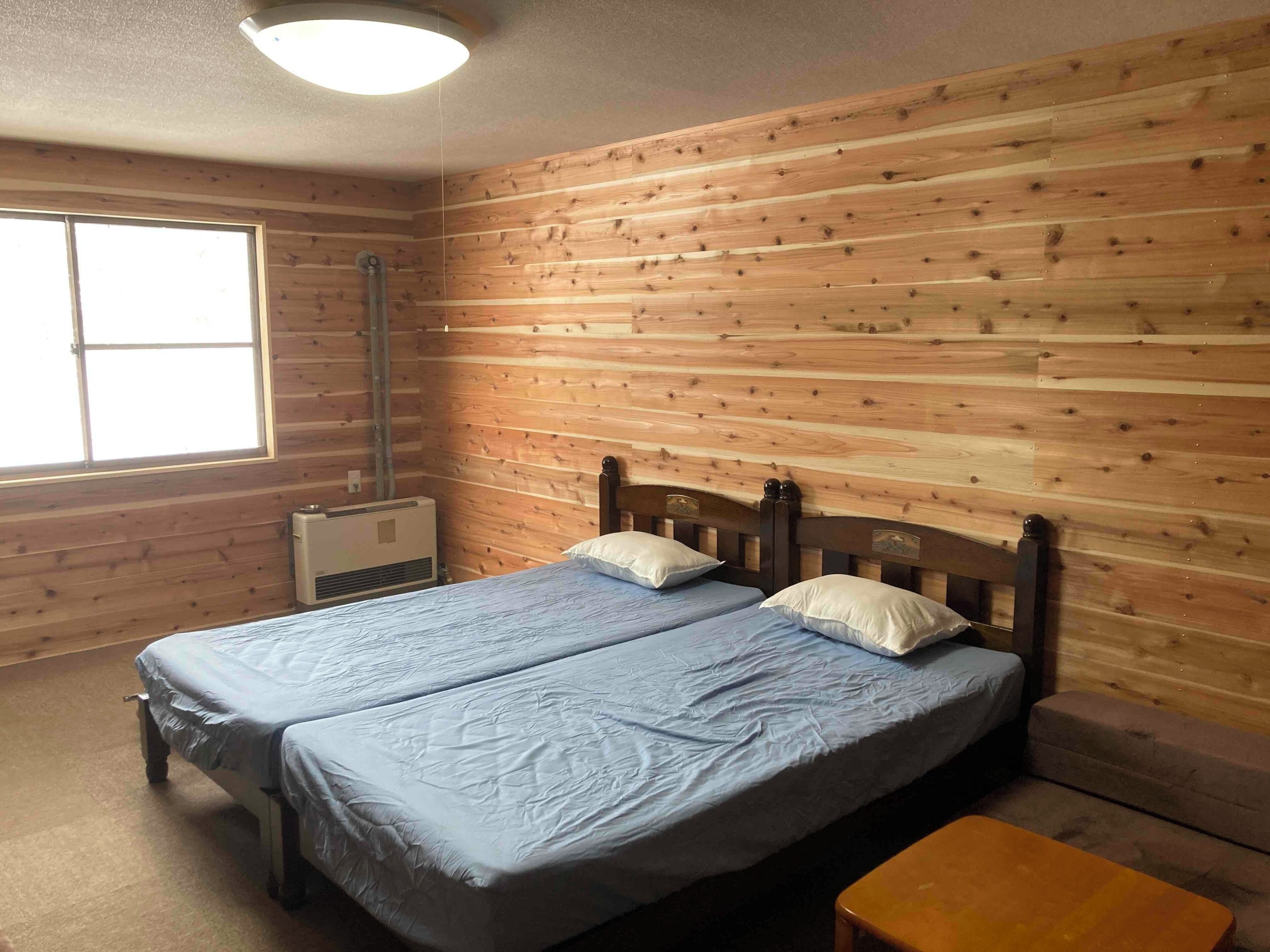A room with two beds, wooden walls, a window, and an air conditioning unit.
