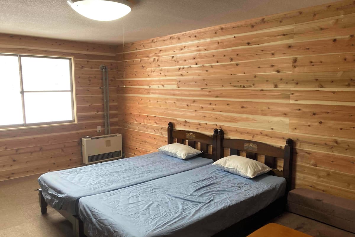 A room with two beds, wooden walls, a window, and an air conditioning unit.