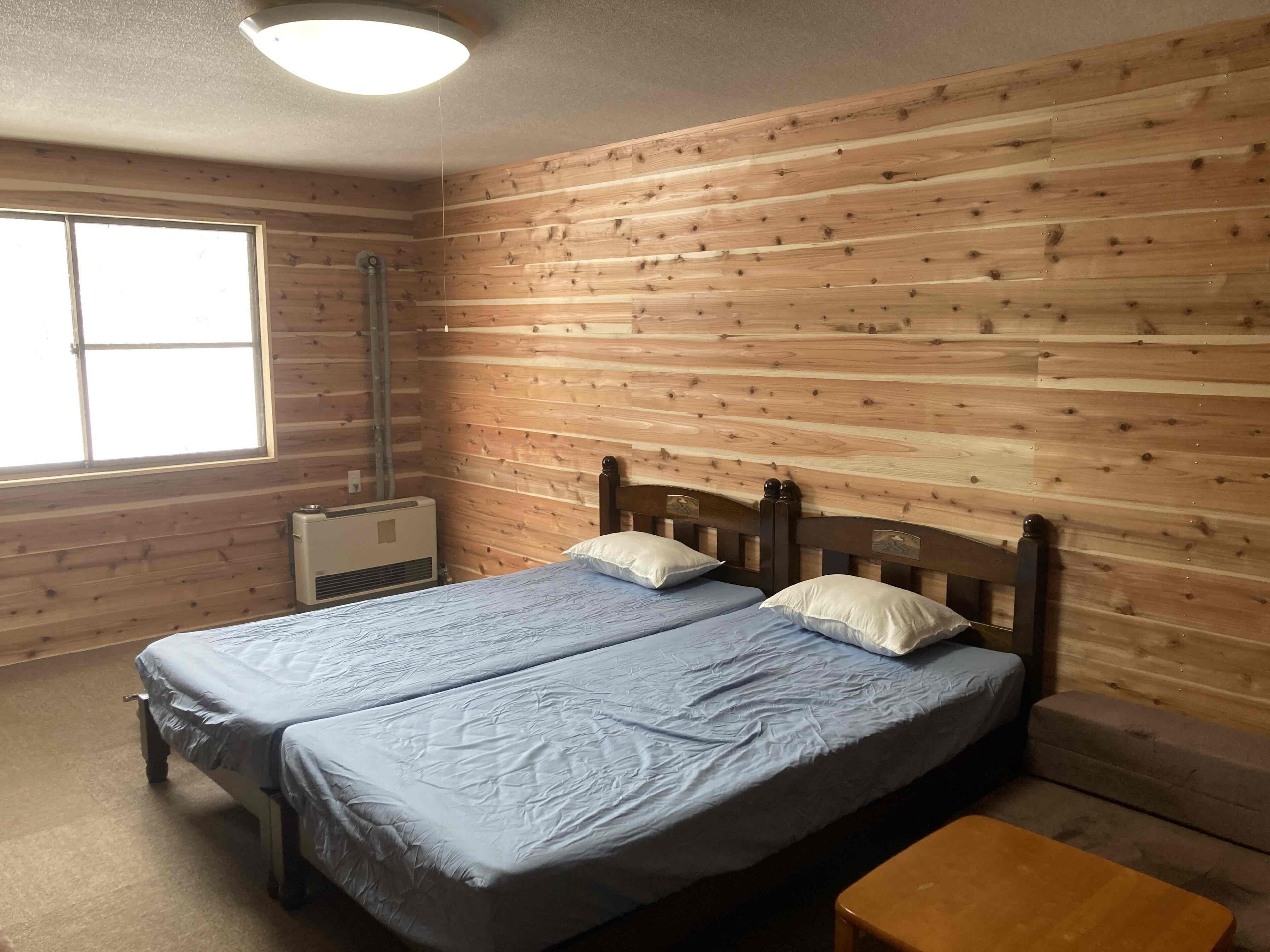 Una habitación con paredes de madera, una cama con dos almohadas, una ventana y un calentador.
