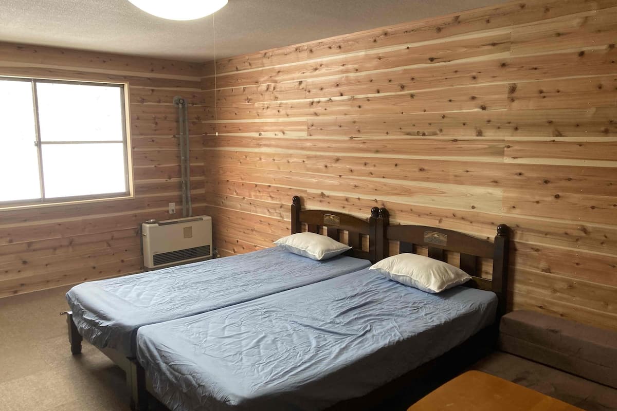 A room with wooden walls, a bed with two pillows, a window, and a heater.