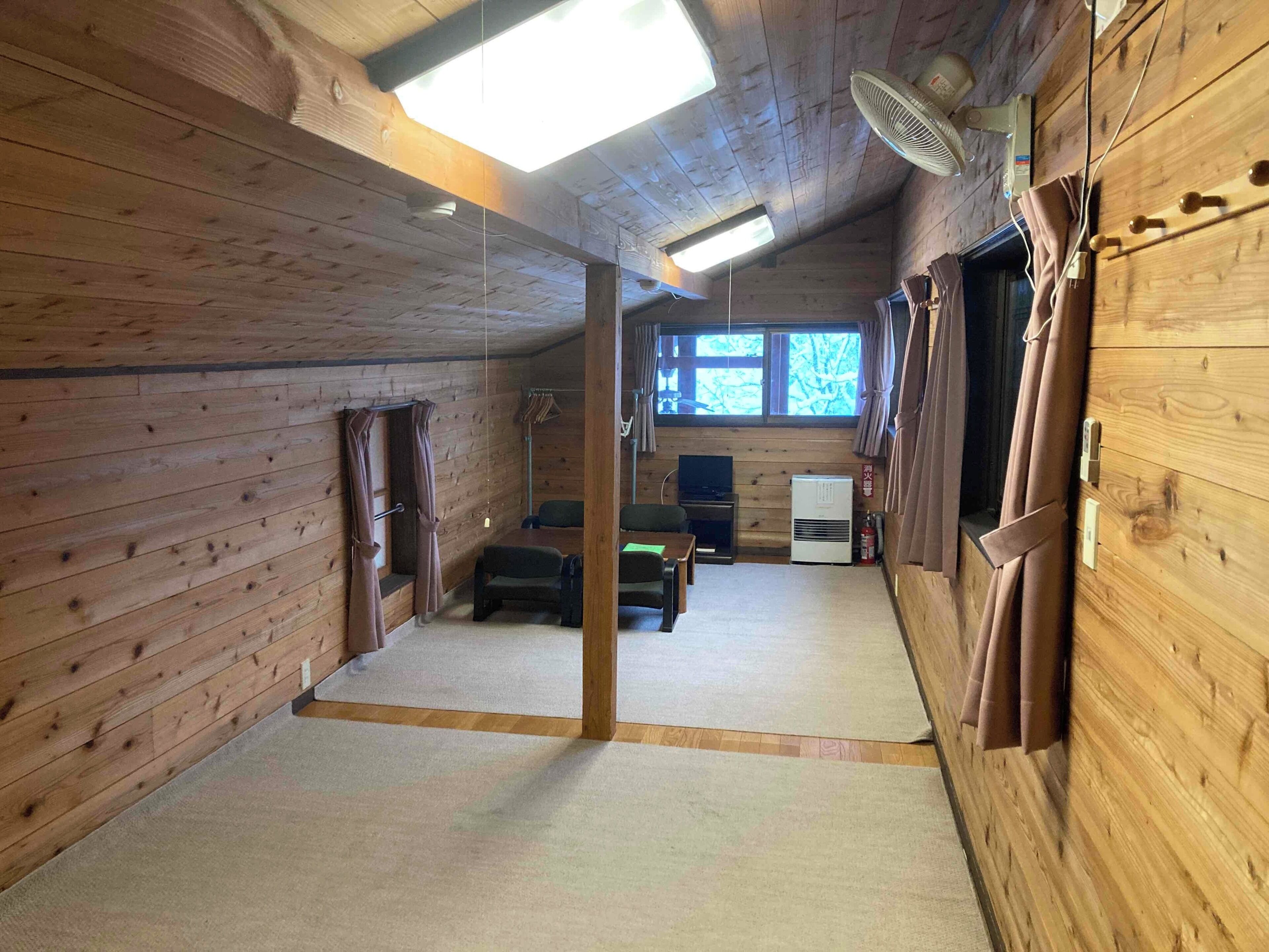A wooden cabin interior with a ceiling fan, a television, and a window with curtains.