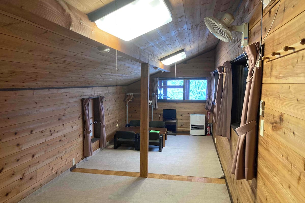 A wooden cabin interior with a ceiling fan, a television, and a window with curtains.